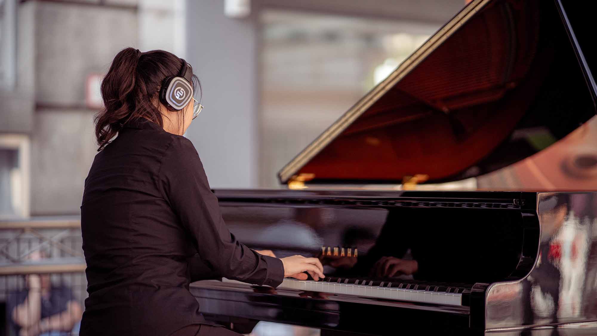 Pianista con auriculares inalámbricos y piano Yamaha en un concierto con audio inmersivo Conciertos de piano con auriculares inalámbricos: guía completa
